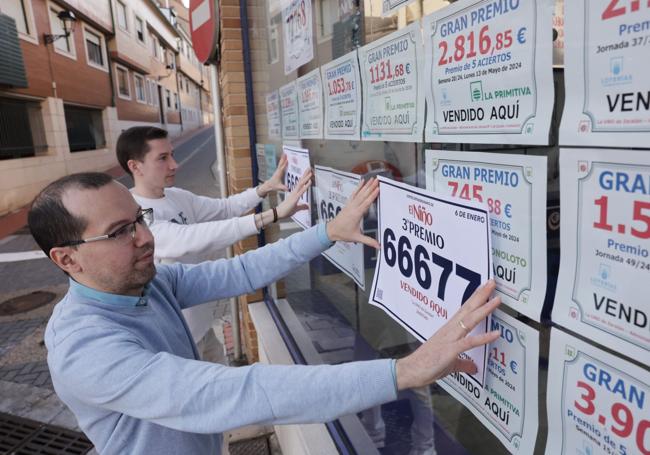 Los hermanos Marcos y Andrés Martínez, del despacho de Zaratán, colocan el cartel con el número que les han distribuido de forma errónea.