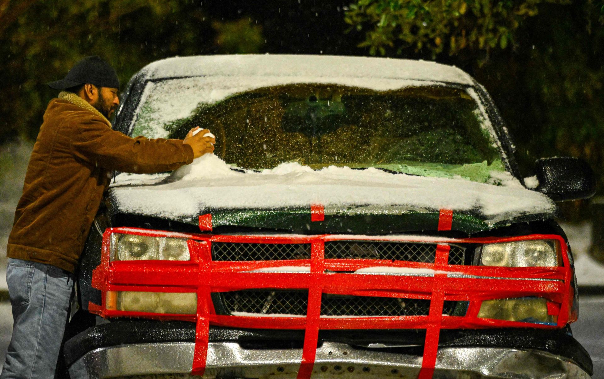 Un hombre quitando nieve de su coche