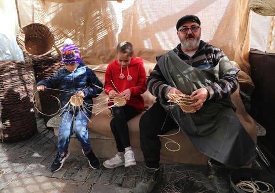 El artesano enseña las técnicas de cestería a dos niños, este lunes en la Plaza Mayor.