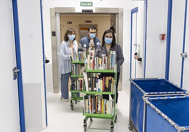 Tres voluntarios de Cadenas de Sonrisas recorriendo los pasillos del clínico cargados de libros