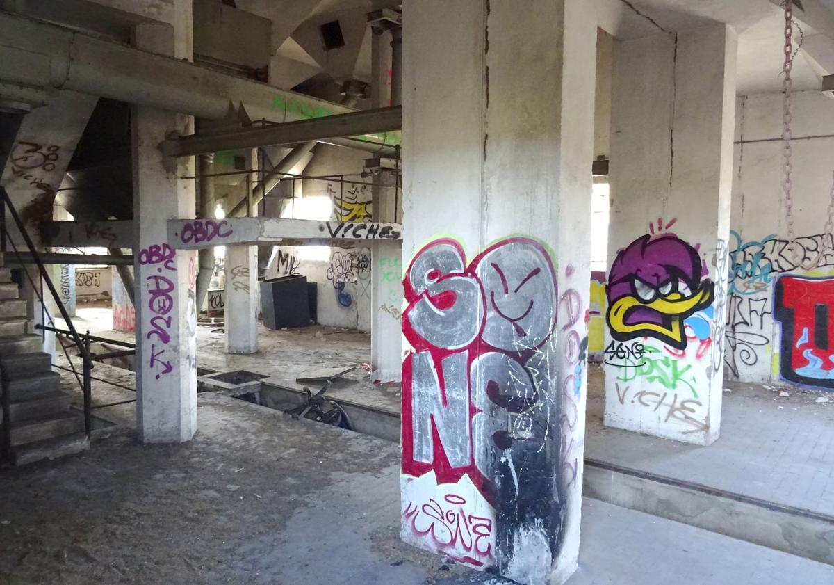 Imagen principal - Planta baja del silo de la avenida de Gijón, repleta de gratis, y frecuentada por menores y grafiteros y detalle (debajo a la izquierda) de las ventanas rotas para salir al tejado en su parte superior. A la derecha, boquete abierto en la valla de la parte posterior de la parcela para acceder a su interior.