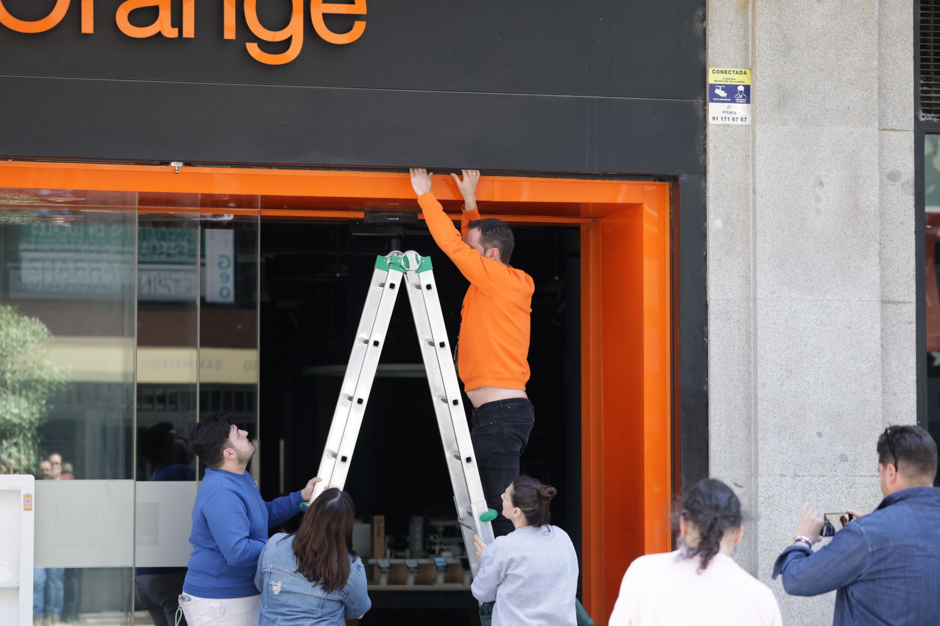 Empleados y responsables de una tienda de Orange intentan bajar manualmente la reja, atascada ante la falta de suministro.
