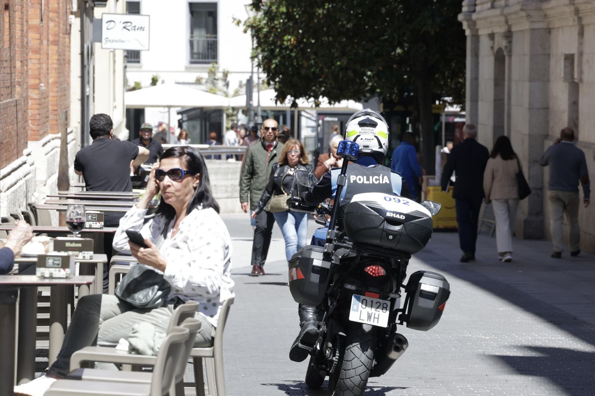 Un motorista de la policía local atraviesa la calle Jesús ante varios ciudadanos ocupando la terraza de un establecimiento hostelero.