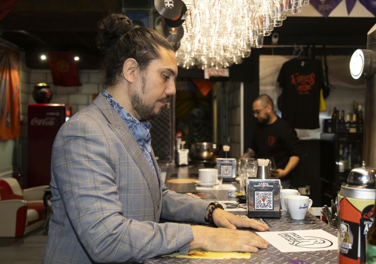 Imagen principal - Max Verdié mira la barra de Faroles Rock, donde aparece su nombre entre el de otros artistas, y posa en una de sus mesas.