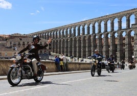 Motoristas vesstidos de traje saludan en su ruta por la ciudad de Segovia.