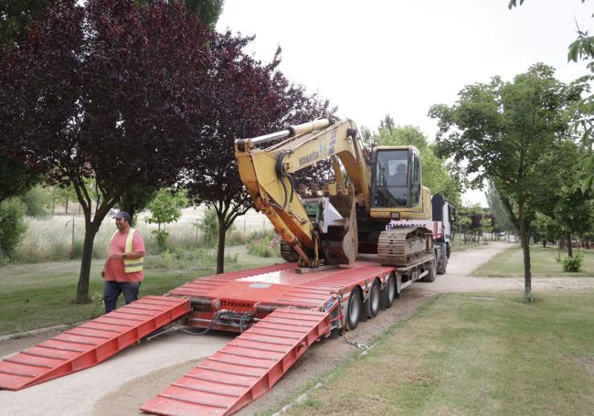 Operarios descargan una retroexcavadora para iniciar las obras en esta pieza de suelo.