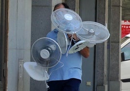 Una persona camina por la ciudad de Segovia con tres ventiladores.