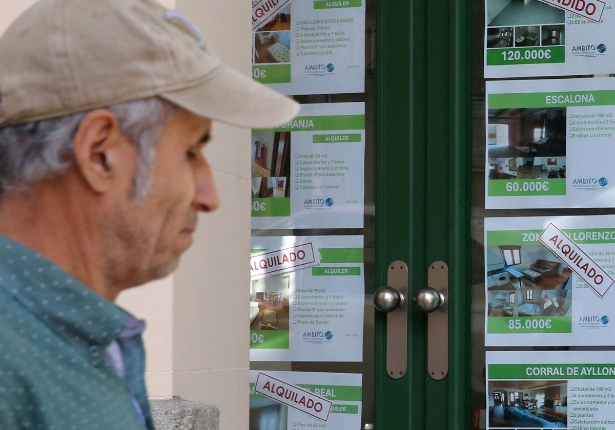 Un hombre pasea junto al escaparate de una inmobiliaria donde se anuncian viviendas en alquiler.