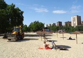 Las máquinas esparcen la arena por la playa de Las Moreras mientras dos usuarios toman el sol en el mobiliario estrenado el pasado verano.