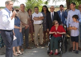 Los maestros María Josefa Díaz, en silla de ruedas, y su esposo Manuel Perucho, de pie a su lado, escuchan las palabras del alcalde de Íscar durante la inauguración de su calle.