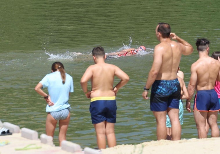 Un grupo de usuarios, al borde del agua en la playa de Las Moreras, mientras dos deportistas cruzan a nado ante ellos.