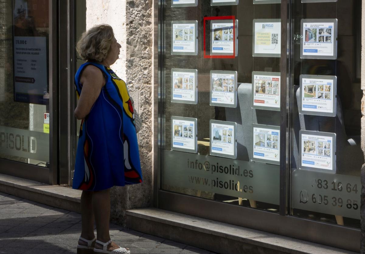 Una mujer contempla los carteles de un escaparate de una inmobiliaria que anuncian pisos en alquiler y venta en Valladolid.