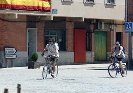 Dos personas pasean en bicicleta por un pueblo de Segovia durante los meses de verano.