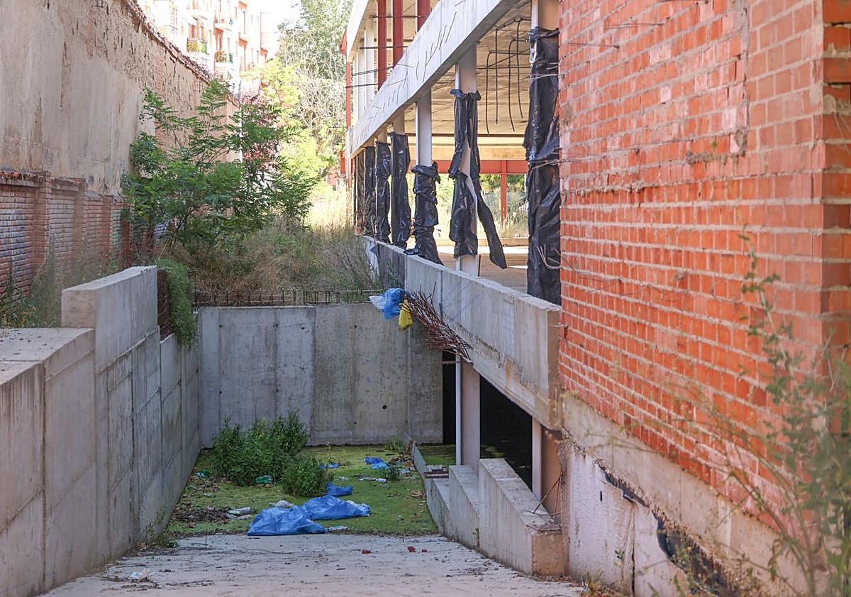 Imagen principal - Verdín y basura en el sótano del inmueble, la valla descolorida que muestra el aspecto que debería tener y pilares desnudos de la estructura.