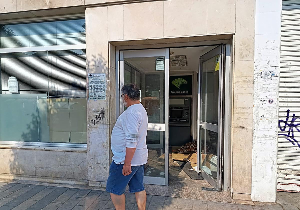 Un hombre pasa por el cajero donde pernoctan varias personas sin hogar en la calle Embajadores.