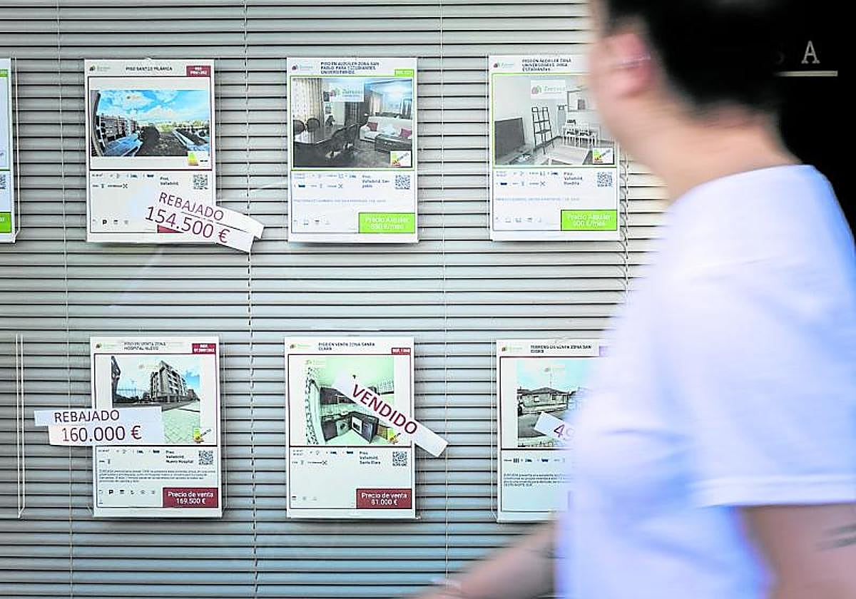 Un joven pasa junto al escaparate de una inmobiliaria con varios pisos a la venta.