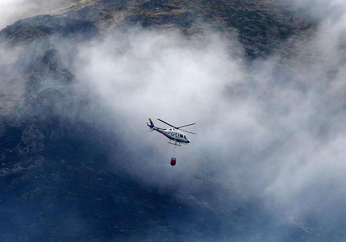 Un helicóptero esparce agua, este lunes, sobre los puntos calientes del incendio de Cerezo de Arriba volando entre el humo y las nubes.