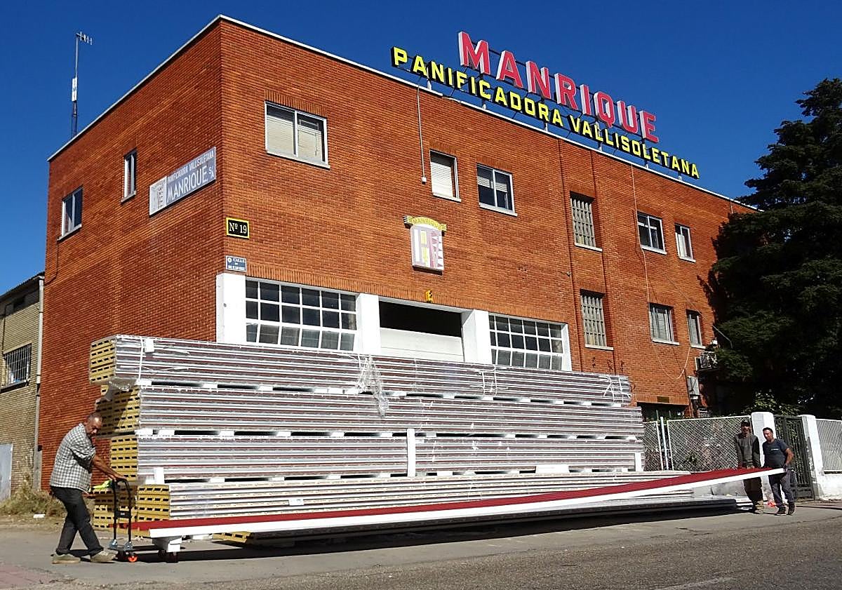 Imagen principal - Los operarios mueven los paneles de la cubierta en las instalaciones para meterlas por el lateral de la nave. Debajo, a la izquierda, detalle del logo de la panificadora.