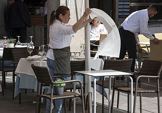 Una camarera extiende un mantel en una mesa de una terraza de la capital segoviana.