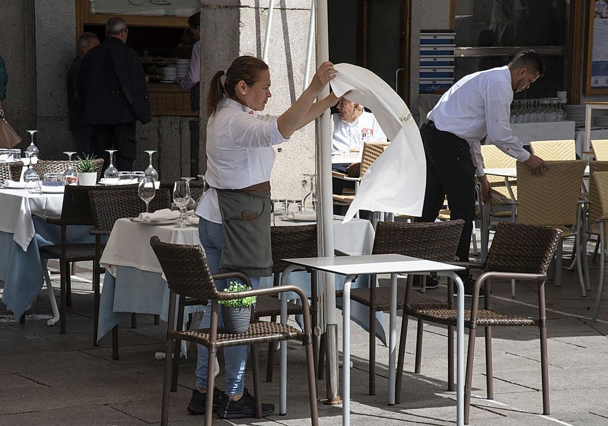Una camarera extiende un mantel en una mesa de una terraza de la capital segoviana.
