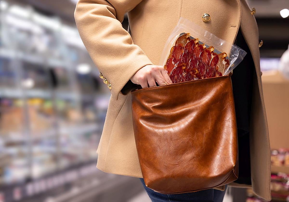 Una mujer introduce un sobre de embutido ibérico en su bolso en un supermercado.
