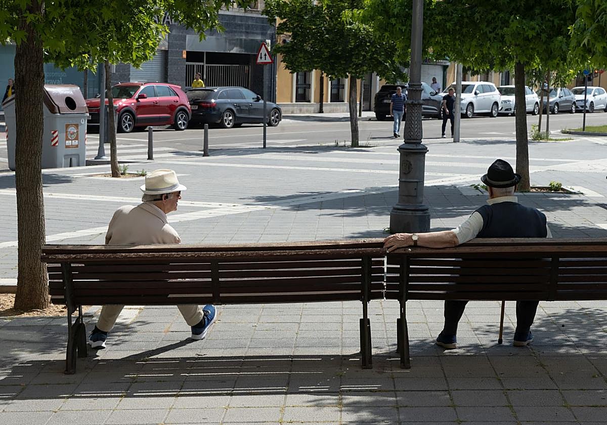 Dos personas sentadas en unos bancos de la calle Recondo.