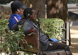 Dos de los migrantes que esperan cita para la Comisaría de Policía sentados en un banco de los Jardinillos de San Roque.