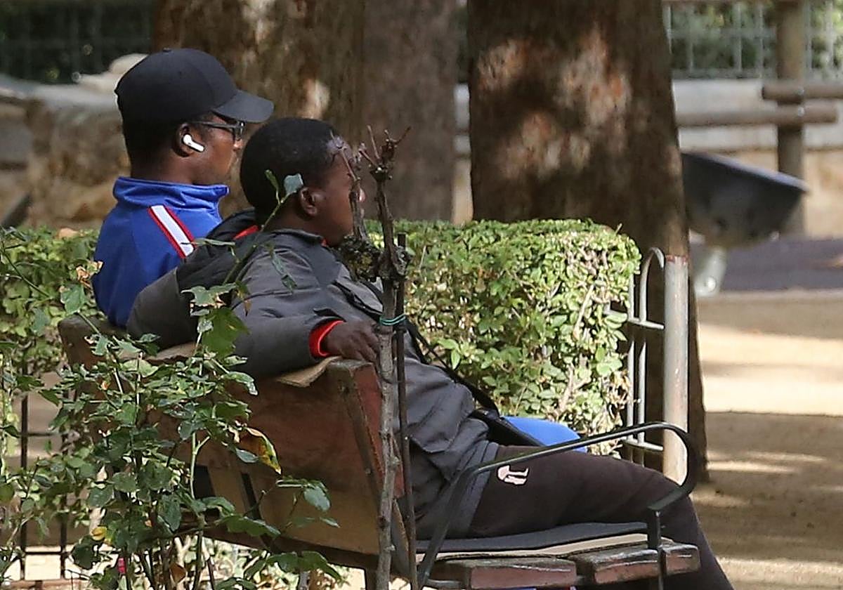 Dos de los migrantes que esperan cita para la Comisaría de Policía sentados en un banco de los Jardinillos de San Roque.