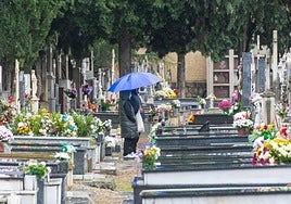 Dos personas se resguardan bajo un paraguas en el cementerio.
