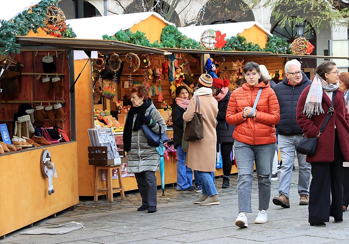 Varias personas caminan por el mercado de Navidad en la Plaza Mayor de Segovia.