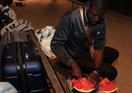 Uno de los subsaharianos solicitantes de asilo come sandía en un banco de San Roque junto a unas maletas y bolsas.