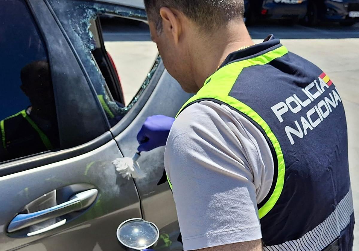 Un agente busca huellas en un coche con la ventanilla rota.