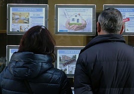 Una pareja observa los carteles de una agencia inmobiliaria que anuncian pisos en venta.