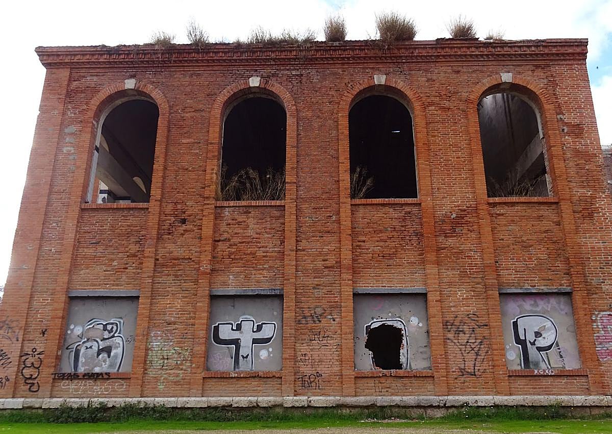 Imagen secundaria 1 - Arriba, las palomas sobrevuelan el inmueble del ala sur de la azucarera Santa Victoria. Debajo, a la izquierda, el frontal en el que se abierto el boquete en una de sus ventanas sobre la 'O' de un grafiti y detalle (derecha) del agujero.