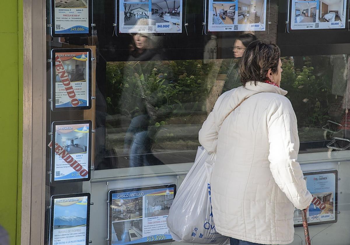Una mujer camina junto a un escaparate con anuncios de viviendas en venta.