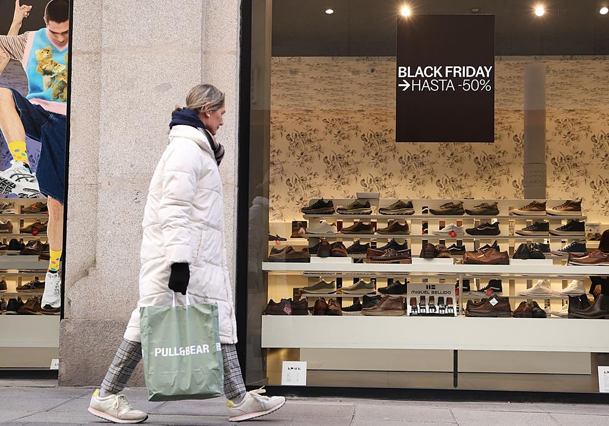 Una mujer camina junto a un escaparate con un cartel del 'Black Friday'.
