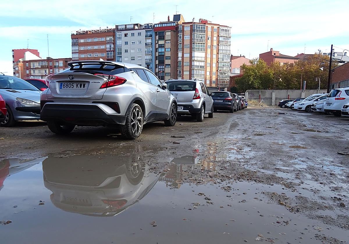 Imagen principal - Arriba, charcos en el firme irregular de la explanada del estacionamiento. Debajo, a la izquierda, el acceso al aparcamiento desde la avenida de Segovia y detalle (derecha) del cartel colocado en la entrada.