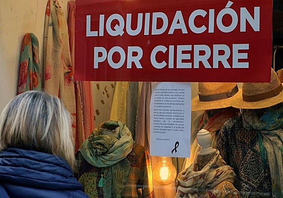 Una mujer se para delante de un escaparate de una tienda de Segovia que anuncia liquidación por cierre.
