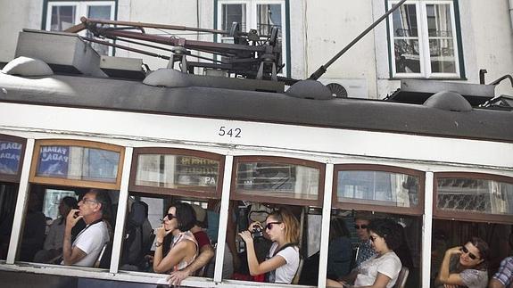 Turistas en Lisboa miran sus dispositivos desde el tranvía. 