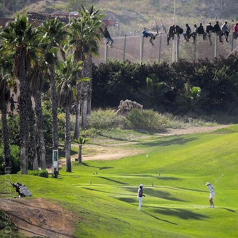 Inmigrantes encaramados a la valla, junto a un campo de golf.