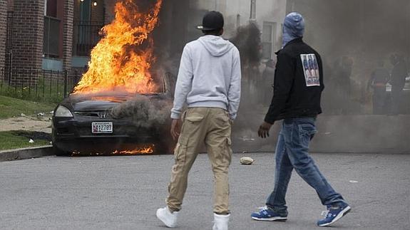 Dos jóvenes observan un vehículo ardiendo. 