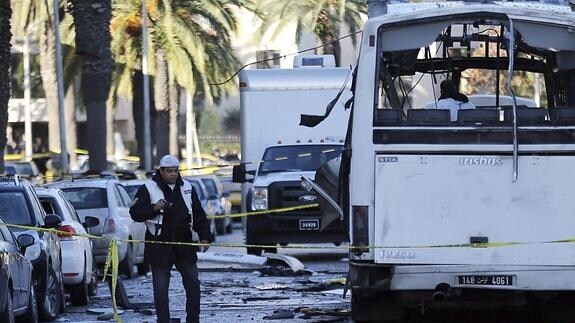 Policías forenses tunecinos inspeccionan los restos de un autobús tras el atentado contra varios guardias presidenciales.