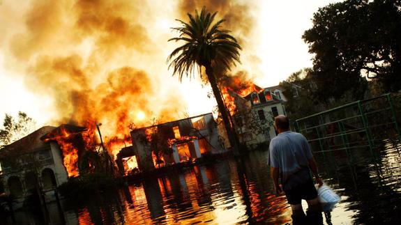 Un hombre con el agua a la altura de las rodillas contempla una casa envuelta en llamas en Nueva Orleans, azotado por el huracán Katrina.