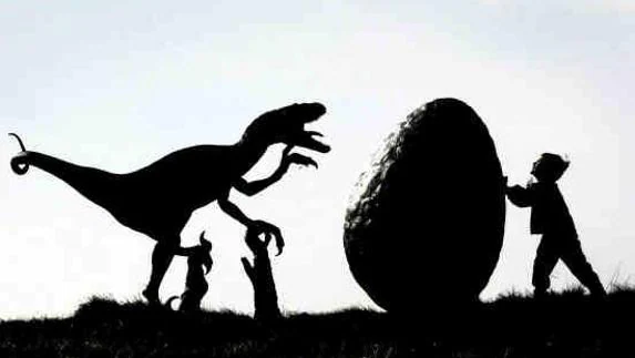 Un niño empuja un huevo de Pascua hacia una figura de dinosaurio. 