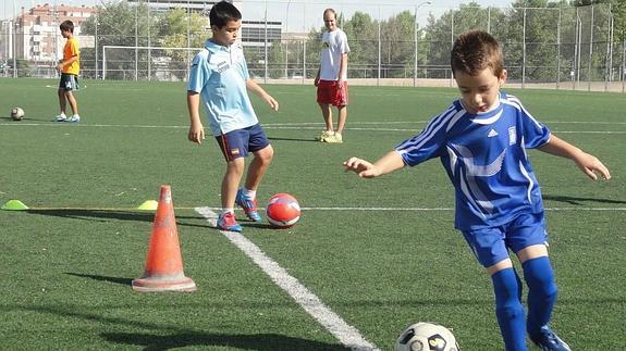 Dos niños se ejercitan junto a un monitor en una escuela de fútbol de Palencia. 