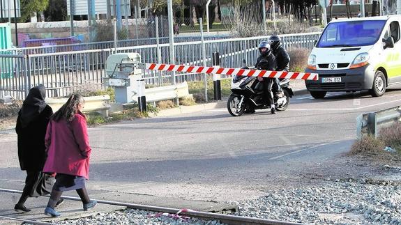 Dos mujeres cruzan ayer a pie el paso a nivel de Los Tres Pasos con la barrera bajada ante el próximo paso de un tren.