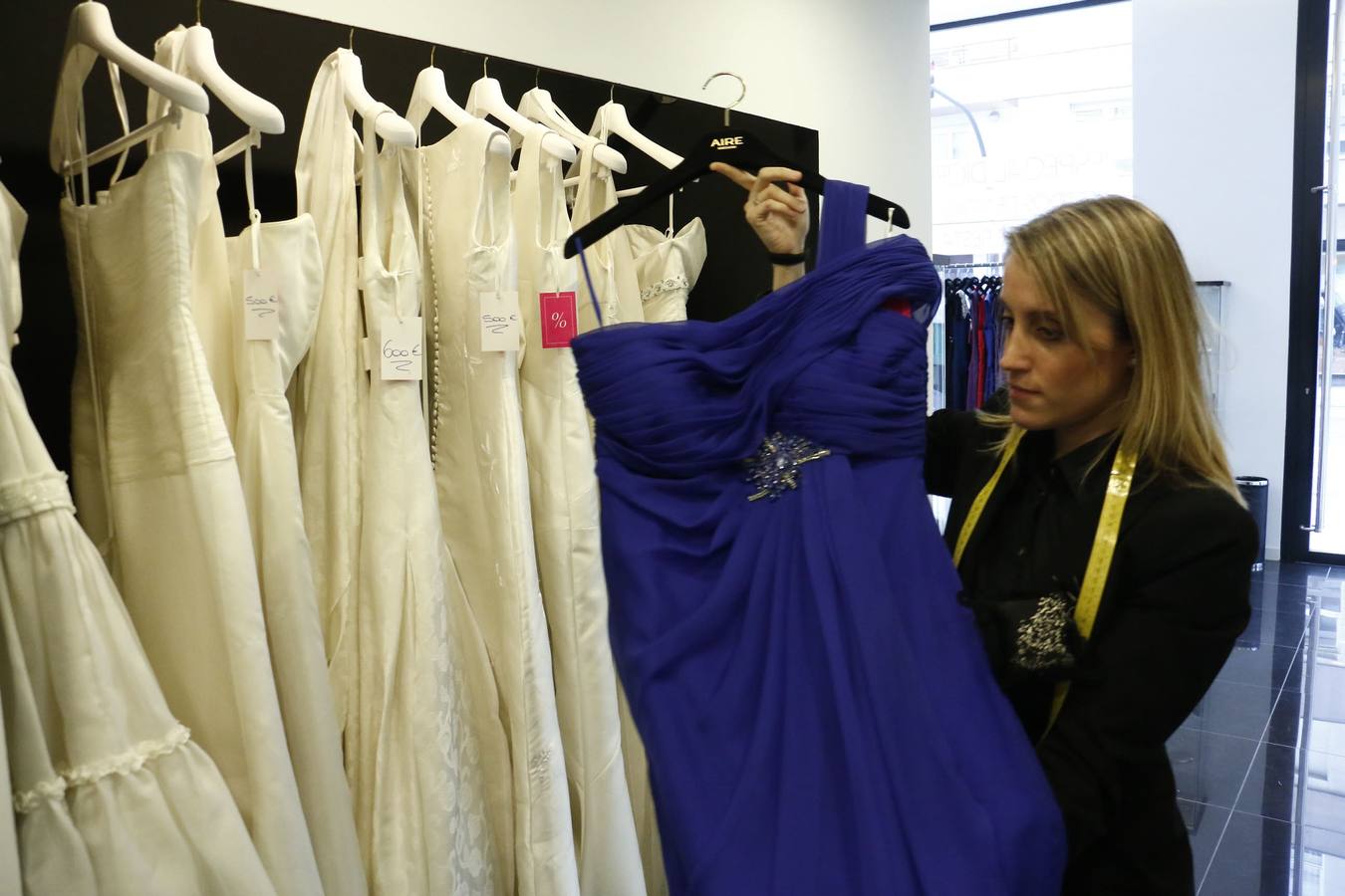 La dependientsa de un comercio muestra varios trajes de novia. 
