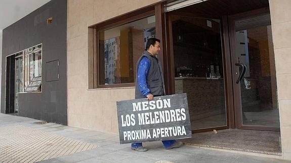 Un obrero, con el cartel anunciador de próxima apertura de un nuevo mesón. 