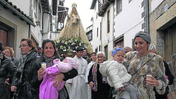 Dos niñas, en brazos de sus madres que portan sendas candelas, participan en la procesión, frente a la Virgen. 