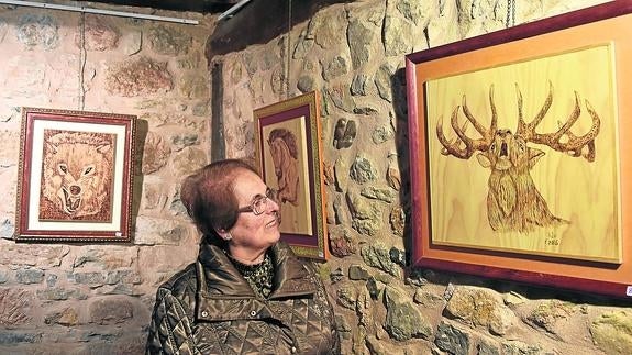 Una mujer visita la exposición de pirograbados en la biblioteca Bernardo el Carpio.
